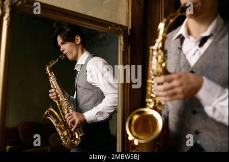 Young man playing saxophone in reflection of mirror at home Stock Photo