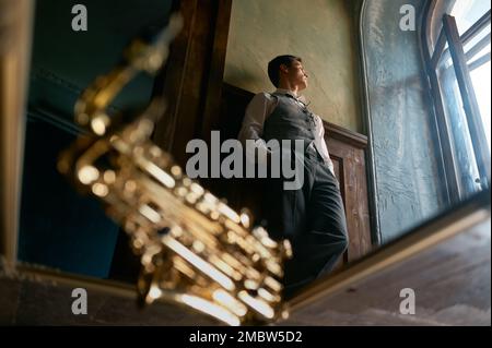 Pensive young saxophonist looking through window view from bottom Stock Photo