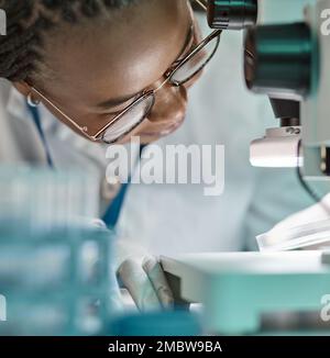 Controlling your experiments is an important part of the scientific method. a young scientist using a microscope in a lab. Stock Photo