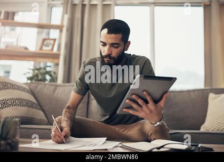 Cleaning up his credit history. a young man using a digital tablet while going through paperwork at home. Stock Photo
