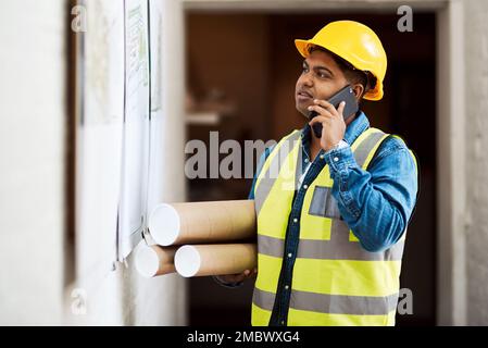 Meet me at the site. a young engineer talking on his cellphone while reading something on a wall. Stock Photo