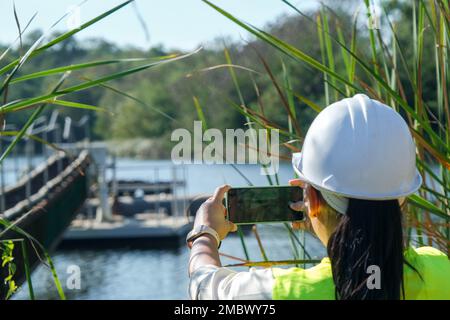 Environmental engineer uses a mobile phone to take pictures and record data analyzing oxygen levels in the reservoir. Water and ecology concept. Stock Photo