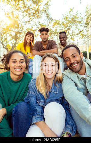 Vertical shot of young student people smiling at camera sitting outdoors Stock Photo