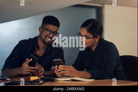 Computer repair service you can count on. two young technicians using their smartphone while repairing computer hardware. Stock Photo