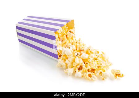 Tasty cheese popcorn falling out of a purple striped carton bucket, isolated on white background. Scattering of popcorn grains. Movies, cinema  and en Stock Photo