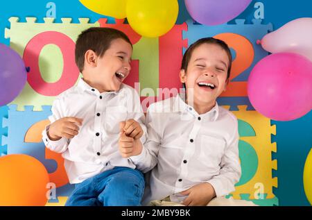 Shot of a cute children lying on the floor among colored balloons in the inner courtyard in white shirts Stock Photo