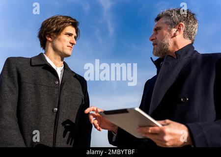 Low angle of focused businessmen in formal wear looking at each other while talking about details of project during meeting on street Stock Photo