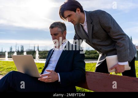 Focused businessmen in formal wear surfing internet while working on laptop remotely from park Stock Photo