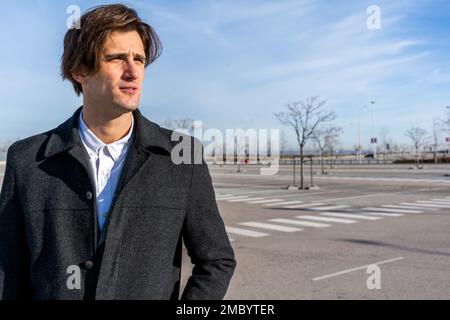 Thoughtful adult businessman in classy coat standing on street and looking away pensively while thinking about new startup project Stock Photo