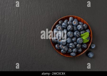 Fresh blueberries on a wooden plate over black slate background. Tasty summer berries. Sweet wild berries for vitamin vegan snack,  vegetarian dessert Stock Photo