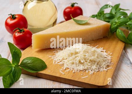 Parmesan and tomatoes on a cutting board. Italian grana padano cheese wedge and grated, red tomatoes, green basil herb and olive oil on wooden surface Stock Photo