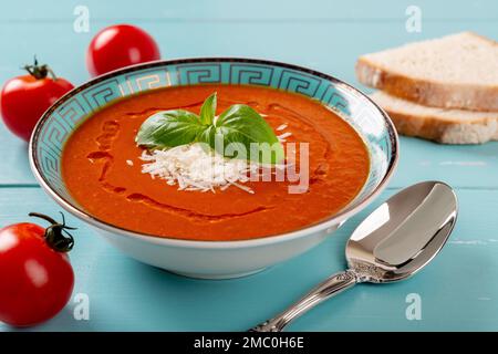 Hot tomato soup and spoon over turquoise wooden table. Homemade soup of pureed tomatoes with grated parmesan and fresh basil. Healthy vegetarian dish. Stock Photo
