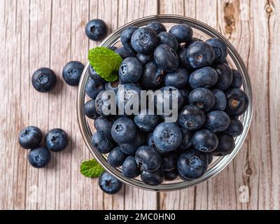 Sweet blueberries in a glass bowl over wooden surface. Ripe juicy wild berry for vitamin vegan snack. Blueberry for natural antioxidant and detox diet Stock Photo