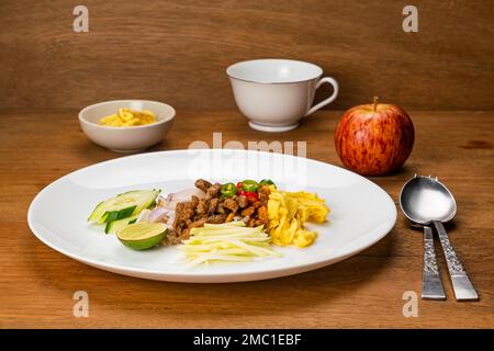 High angle view of shrimp paste fried rice with sweet pork, fried egg and other in white ceramic dish with a cup of coffee and ripe red apple on Stock Photo