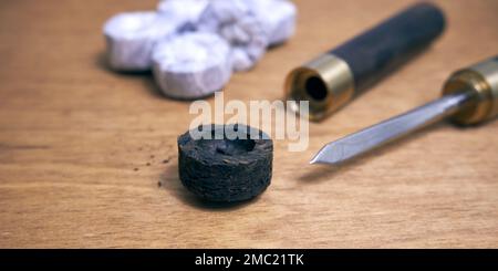 Pu-erh tea in the form of a round pressed briquette and a knife for grinding it on a wooden table Stock Photo