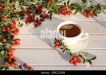 Cup of tea with rose berries on a white wooden background Stock Photo