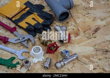 Plumbing tools, parts, pipeline components and gloves on the background of a construction OSB plate. Place for text or logo. Stock Photo