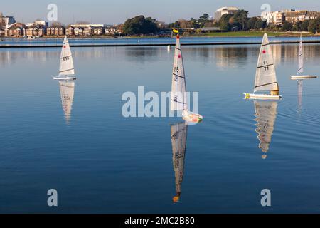 Poole, Dorset UK. 21st January 2023. UK weather: Bitterly cold frosty morning at Poole doesn't deter keen radio controlled boat enthusiasts racing their Laser model boats around Poole Park lake. Little wind and frozen patches makes racing difficult, but create a calm serene scene with beautiful reflections in the sunshine. Credit: Carolyn Jenkins/Alamy Live News Stock Photo