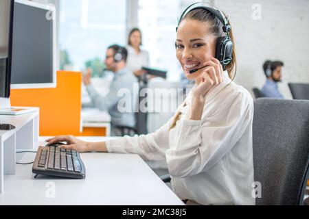 Positive female customer services agent with headset working in call center. Stock Photo