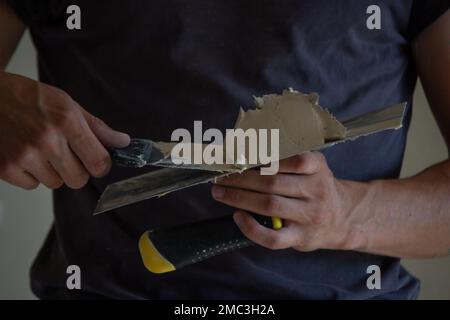 A man holds a spatula with putty in his hands. Selective focus. construction Stock Photo