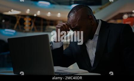 Middle-aged ethnic stressed worried African American man has problem with business papers error laptop trouble bankrupt male 50s businessman with Stock Photo