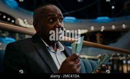 Pensive thinking thoughtful African American man businessman worker entrepreneur rich employer counting money cash dollars budget savings indoors in Stock Photo