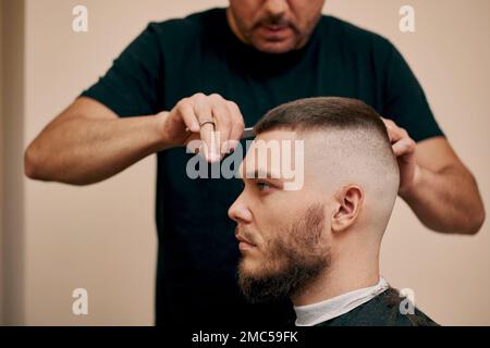 Side view of young bearded man getting haircut in barber shop. close-up Stock Photo