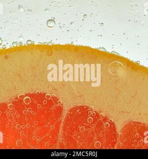 Close-up view of the red grapefruit slice in water background. Texture of cooling fruit drink with macro bubbles on the glass wall. Flat design. Stock Photo