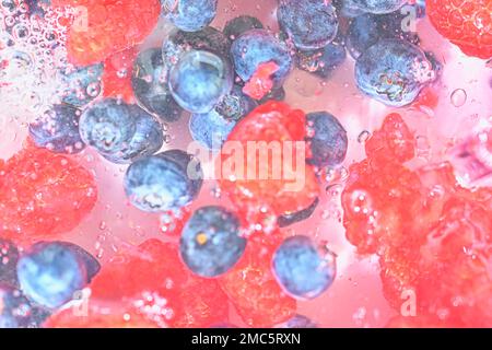 Blueberries and raspberries in liquid with bubbles. Colourful ripe bilberries and raspberries in water. Close-up of fresh berries in water background Stock Photo