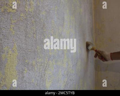 copy space on a textured peeled wall and a painter's hand in a glove with a brush applying a grout to the surface of the wall in blur Stock Photo