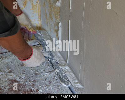 leveling the surface of the room wall with a wide spatula and finishing plaster, working with the finishing solution in the corner of the room Stock Photo