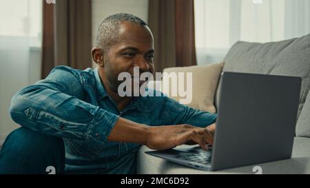 African american middle aged businessman typing laptop mature ethnic male programmer freelancer work remote home in cozy living room smiling man Stock Photo