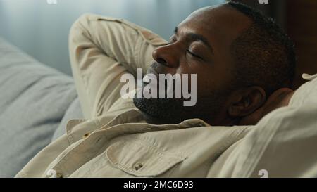Headshot calm relaxed happy african american man relax resting on couch enjoying calmness sleepy lazy male dreamer dozing on comfortable sofa in Stock Photo