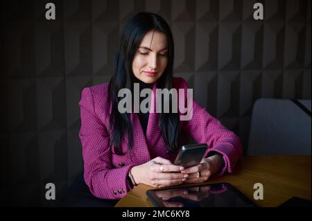 Beautiful confident Caucasian 40-45 years old woman, successful businesswoman in formal wear, chatting on mobile phone while waiting for colleagues an Stock Photo