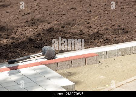 A tool, a rubber mallet for laying paving slabs against the background of a footpath site under construction on a sunny day. Copy space. Stock Photo