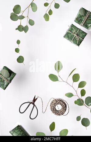 Eucalyptus twigs and gift boxes with wrapping paper isolated on white background. Flat lay, top view overhead. Scissors with reel of stripy gold white Stock Photo