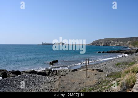 Playa de Triana pebble beach looking toward cement works in Peninsula with El Pajar which locals want to keep and central government want to convert t Stock Photo