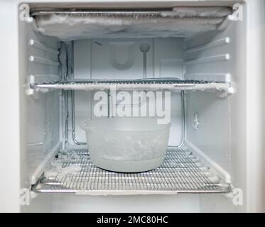 a very icy open freezer is defrosted with a bowl of hot water Stock Photo