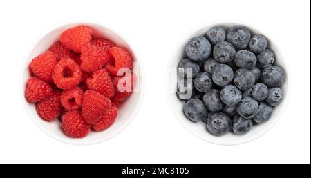 Fresh raspberries and blueberries, in white bowls, from above. Whole and ripe fruits. Stock Photo
