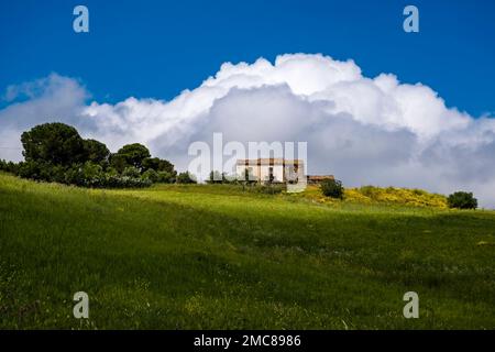 A lonely farmhouse on a hill in Sicilian agricultural landscape near the small town of Collesano, a storm cloud building up behind. Stock Photo