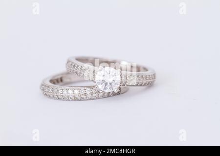 Close up of two white gold / silver rings, one with a large diamond stone, and the other a studded band. Stock Photo