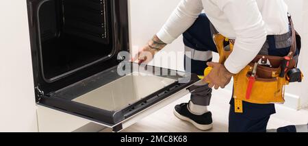 Professional serviceman repairing modern oven in kitchen Stock Photo