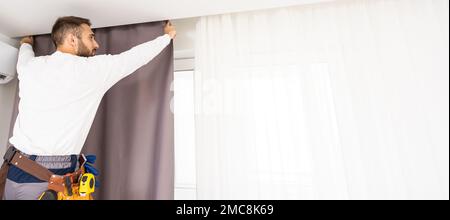 worker repairman hanging and fixing the curtain on the window Stock Photo