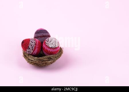 Three knitted Easter decorative eggs in lilac and purple shades in a nest on a purple background. Happy Easter concept. Greeting card with a copy of t Stock Photo