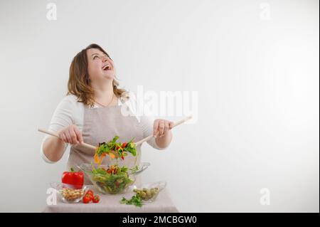 Portrait of happy playful woman eating fresh salad from bowl and winking isolated raised her head and laughs out loud sincerely space for ad cooking blog show banner cook dinner stir salad Stock Photo