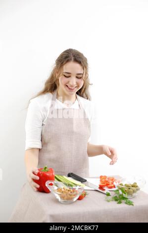 Smiling young woman serving fresh salad on plate. Happy smiling cute woman cooking fresh healthy vegan salad at home with many vegetables in kitchen and trying new recipe High quality photo Stock Photo