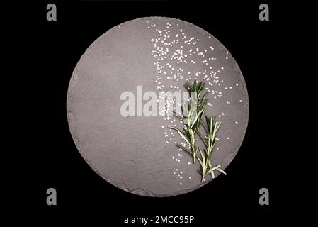 Rosemary herb on a gray stone board in a round shape on an isolated black background Stock Photo