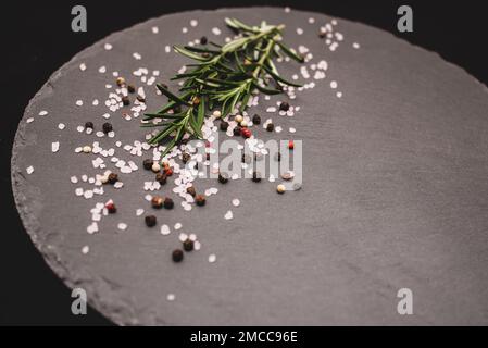 Rosemary herb with pink salt and pepper on gray slate board. Set of various spices for cooking. Stock Photo