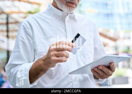 Old senior professional business man holding digital tablet and credit card. Stock Photo