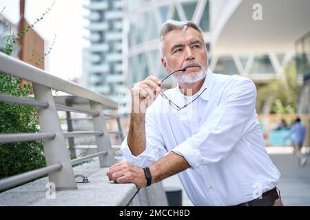 Thoughtful serious older senior business man thinking standing outdoors. Stock Photo